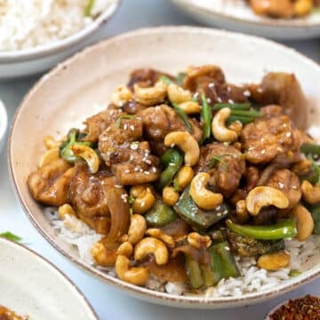 chicken stir fry topped with cashews in a bowl with rice.