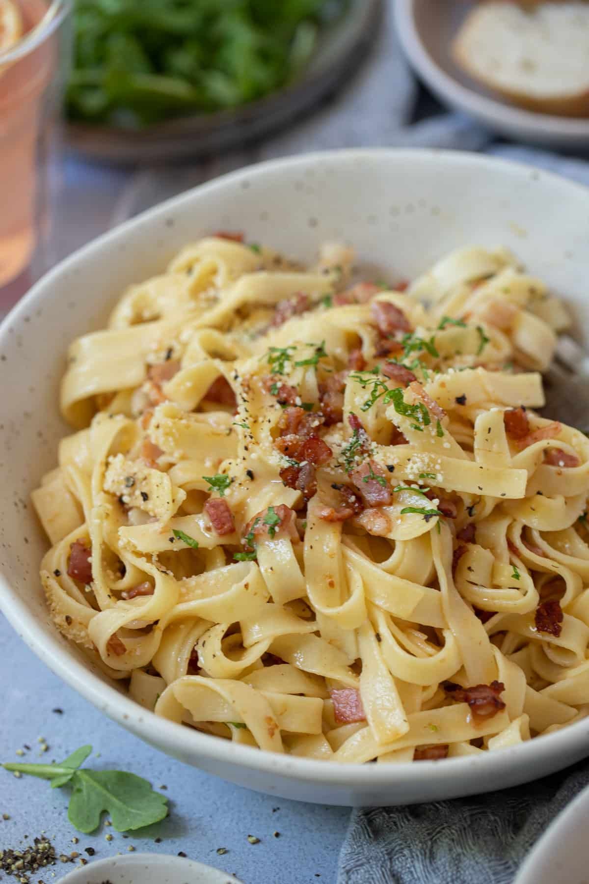 a bowl of fettucine carbonara, topped with bacon and herbs.