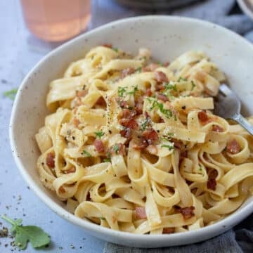 fettucine carbonara in a bowl topped with bacon and herbs.