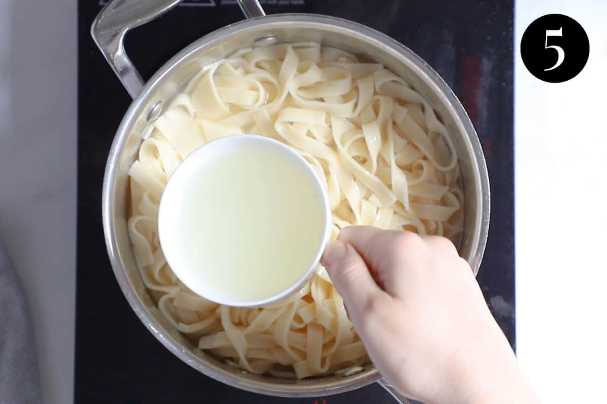 a hand scooping a cup of water from a pot of pasta.