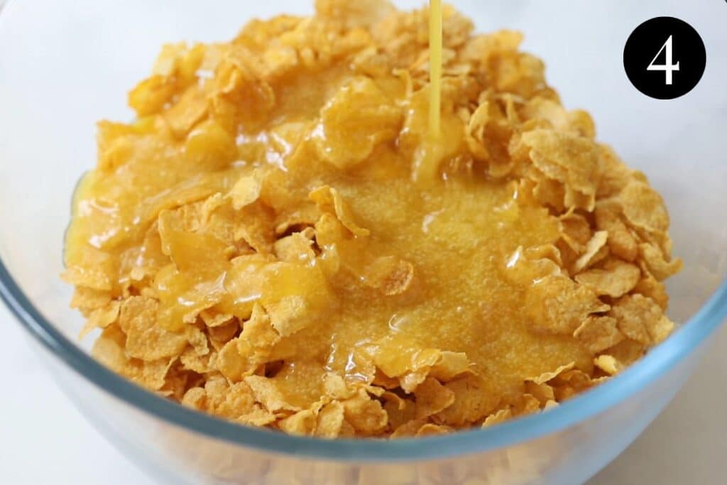 honey mixture being poured over corn flakes in a mixing bowl.