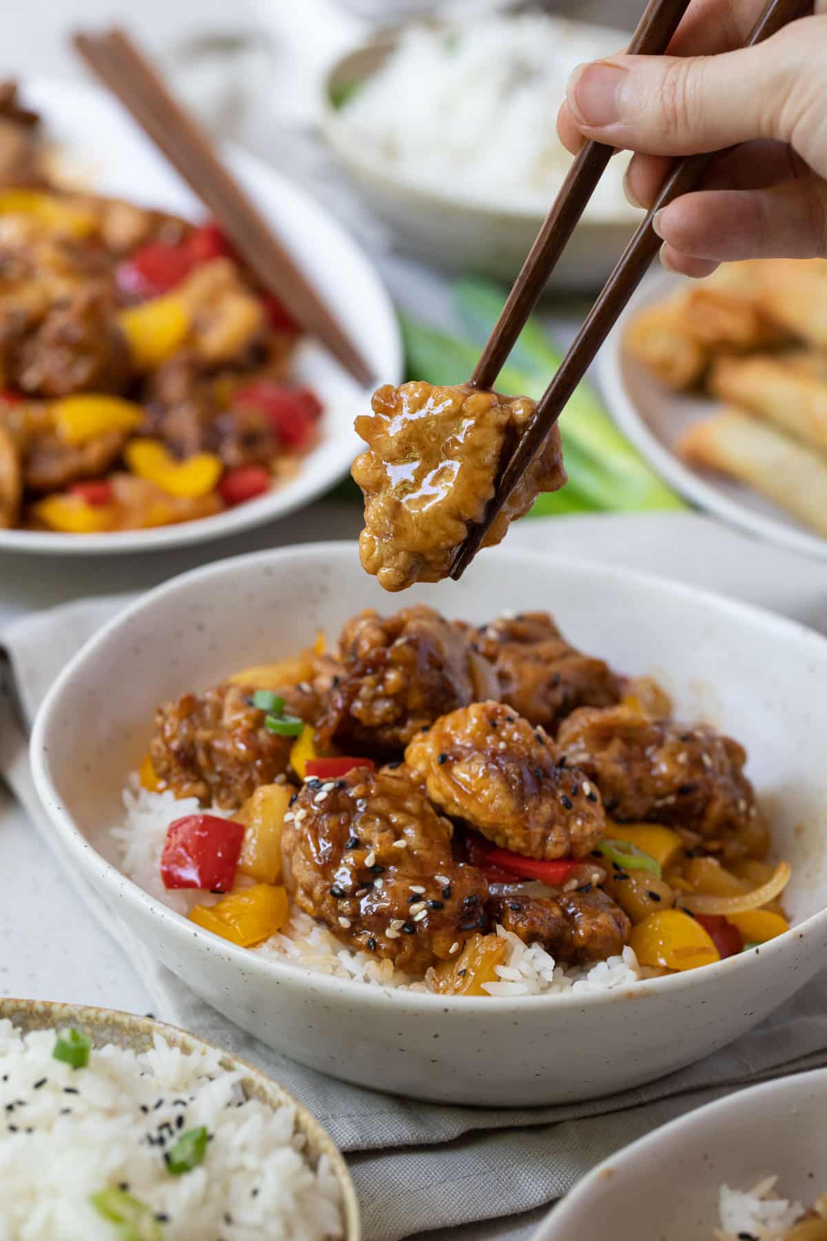 a hand holding chopsticks with a piece of battered pork.