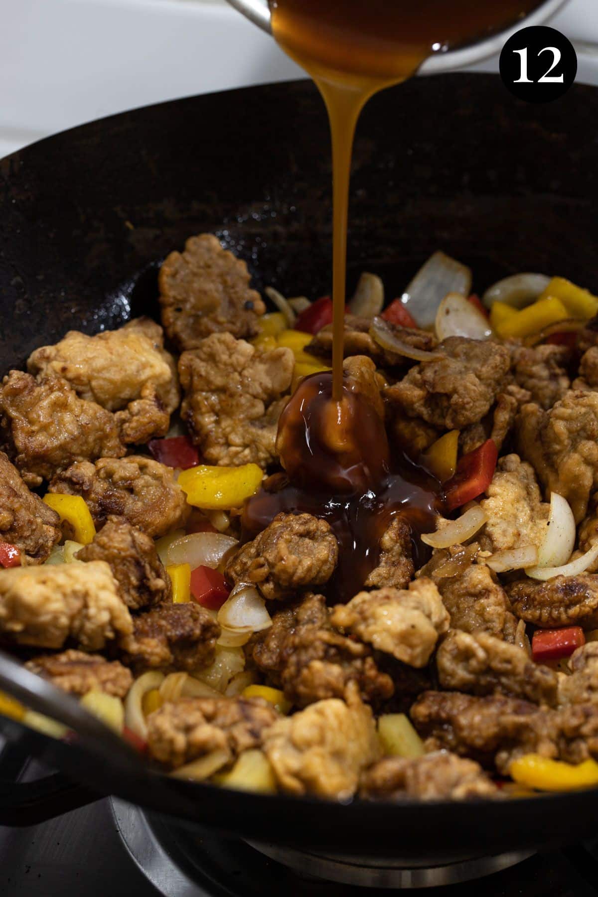 sweet and sour sauce being poured over pieces of pork in a wok.