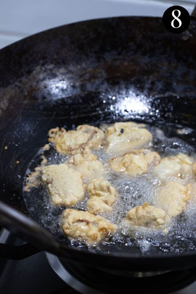 pieces of battered pork, frying in a wok of oil.