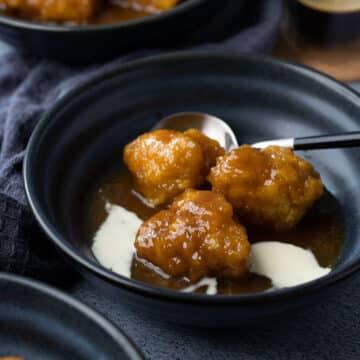 golden syrup dumplings in a bowl topped with cream.