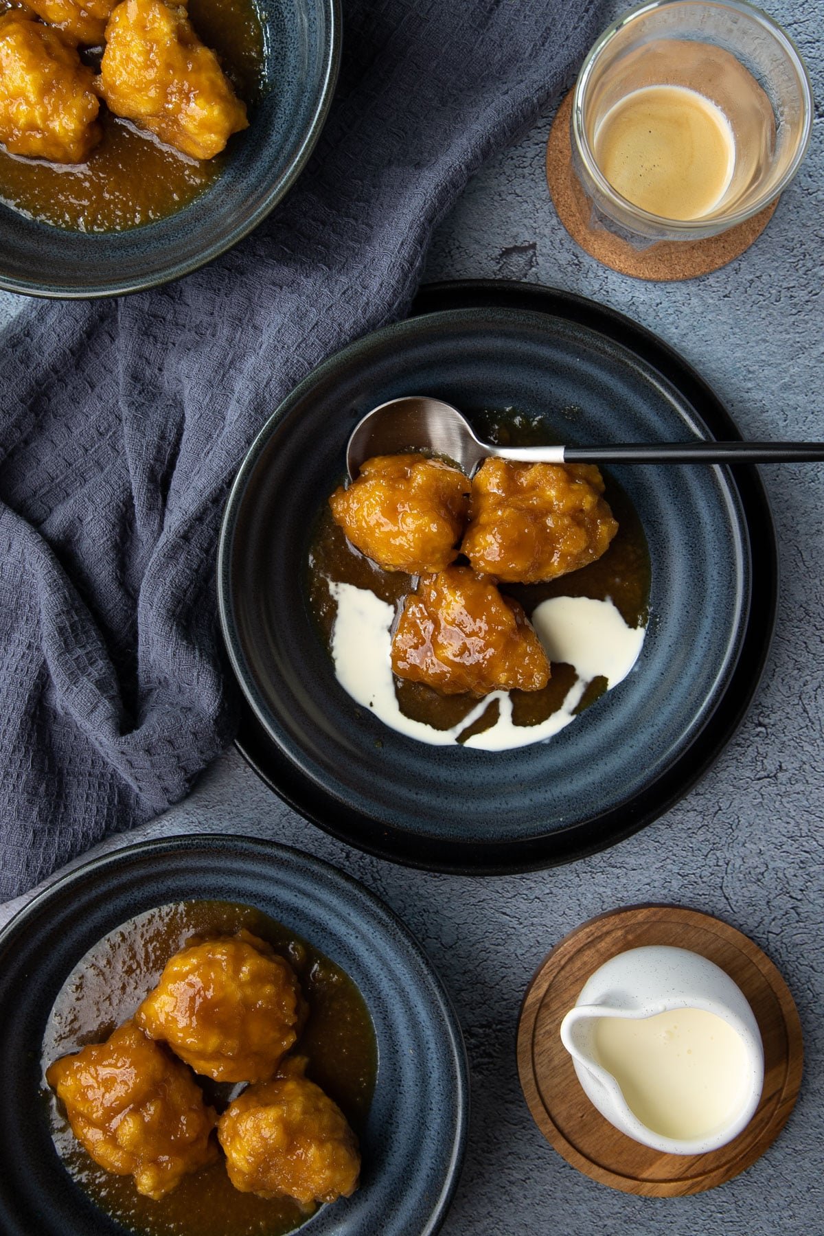 golden syrup dumplings in bowls on a table with cream and coffee.