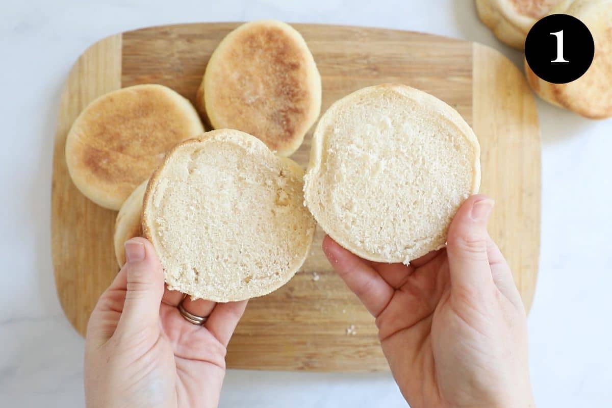 hands holding English muffin halves over a wooden board.