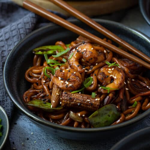 a bowl with prawns, noodles and vegetables, with chopsticks on the side.