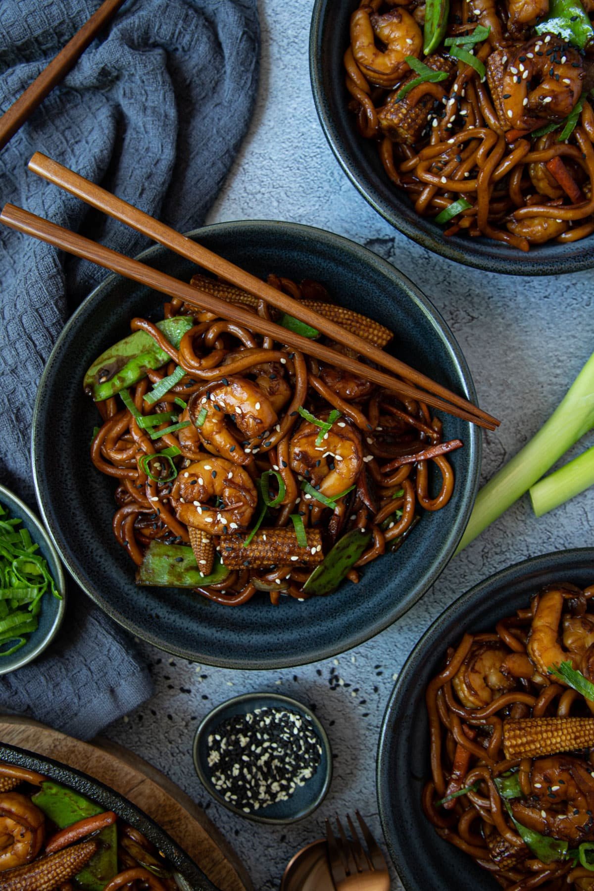 bowls of prawn noodle stir fry, arranged on a table with chopsticks.