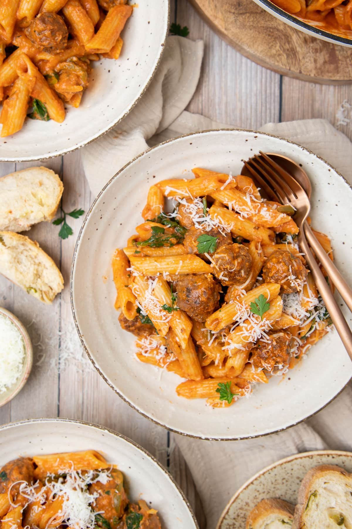 a table topped with bowls of sausage pasta, bread and cheese.