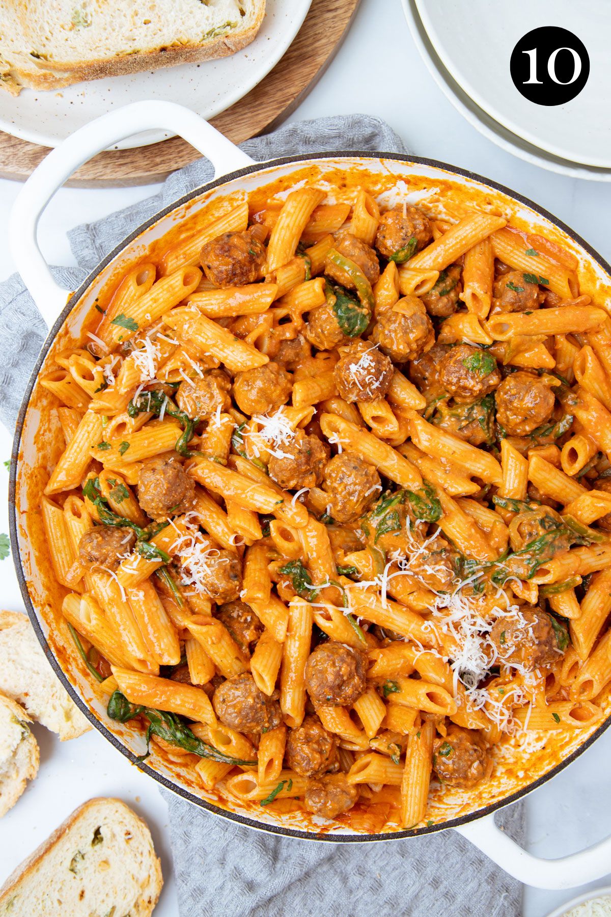 finished sausage pasta in a pan, topped with cheese and spinach.