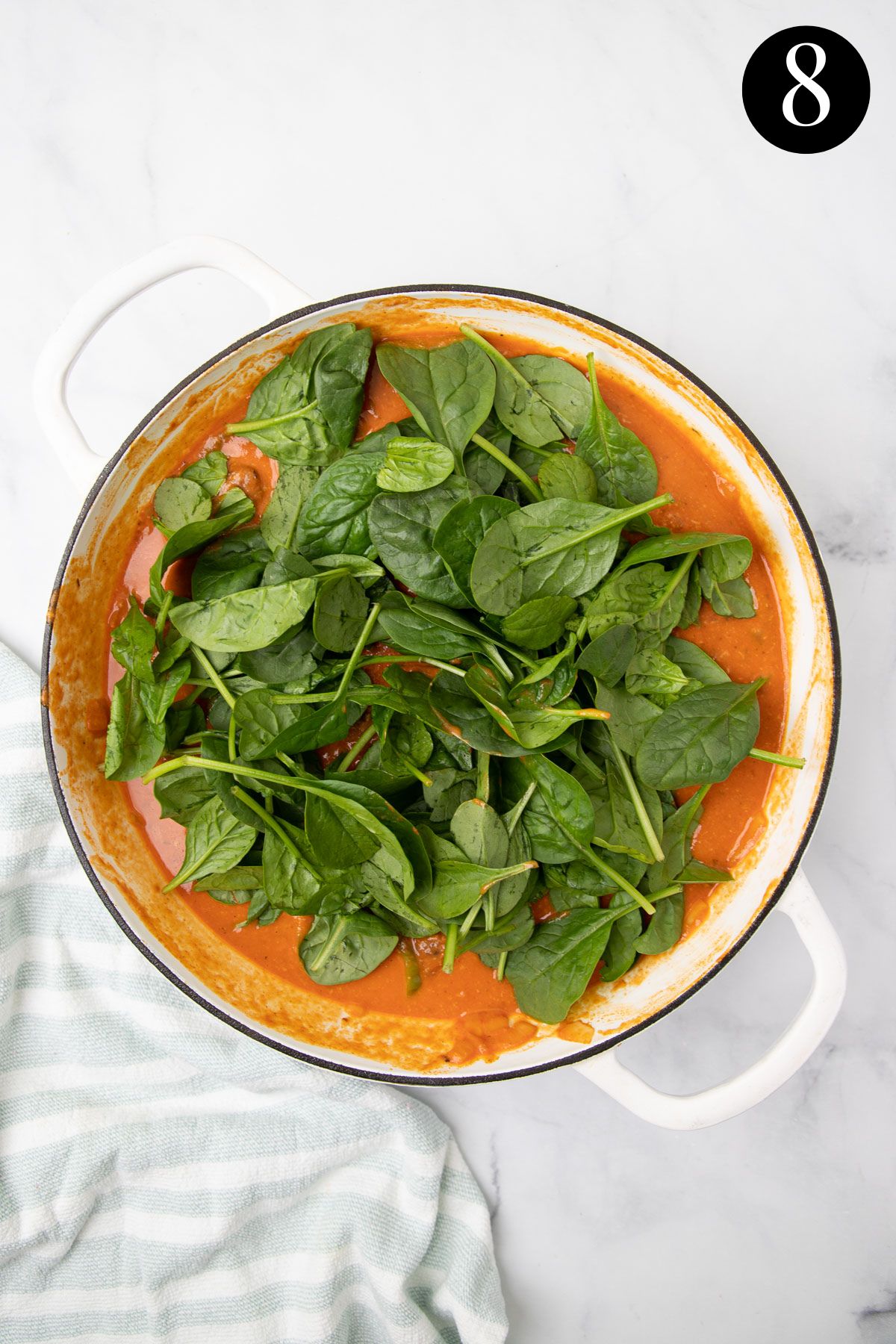 spinach leaves sitting on a pan with tomato sauce.