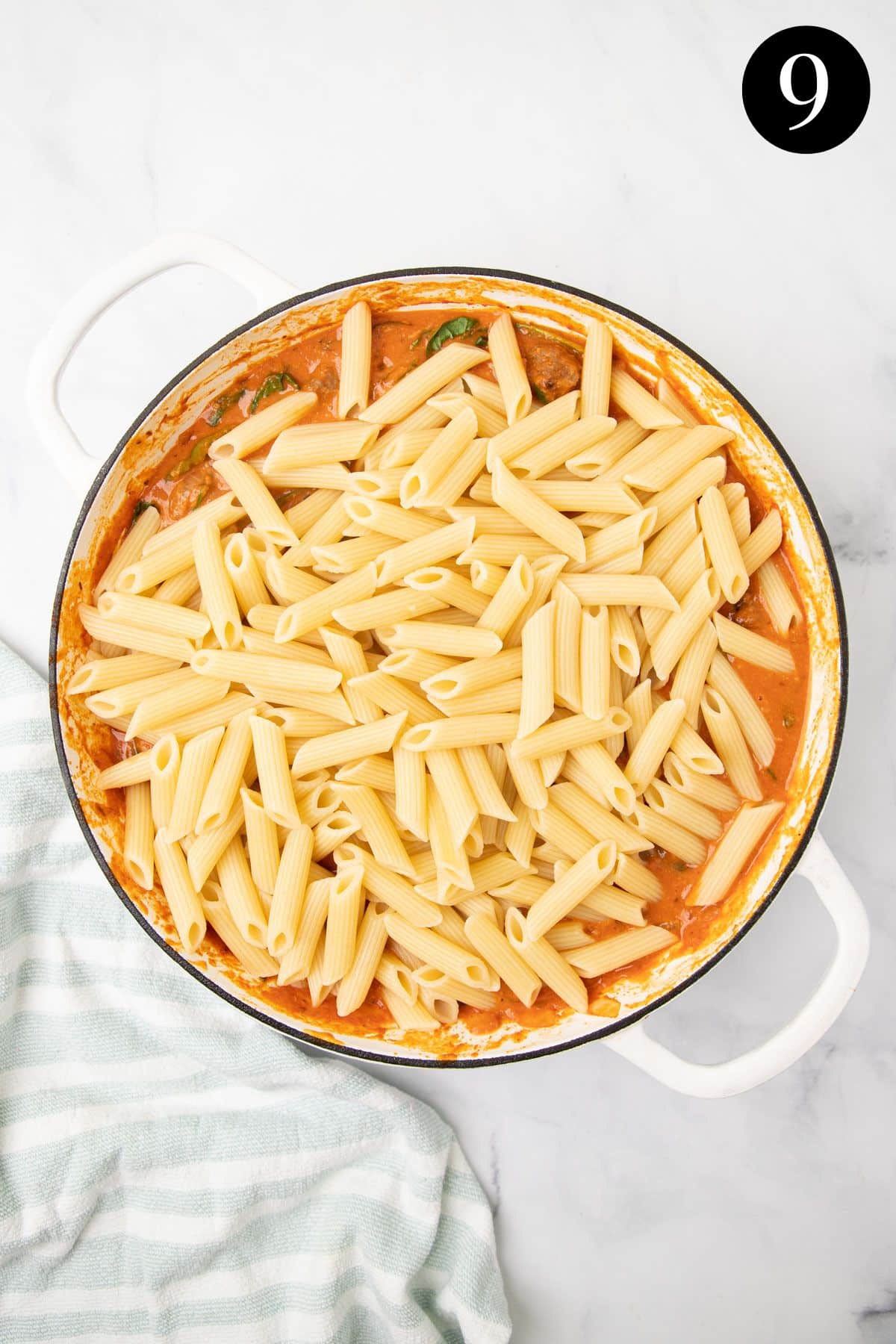 penne pasta on top of tomato sauce in a pan.