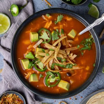 a bowl of Mexican soup topped with tortillas and avocado.