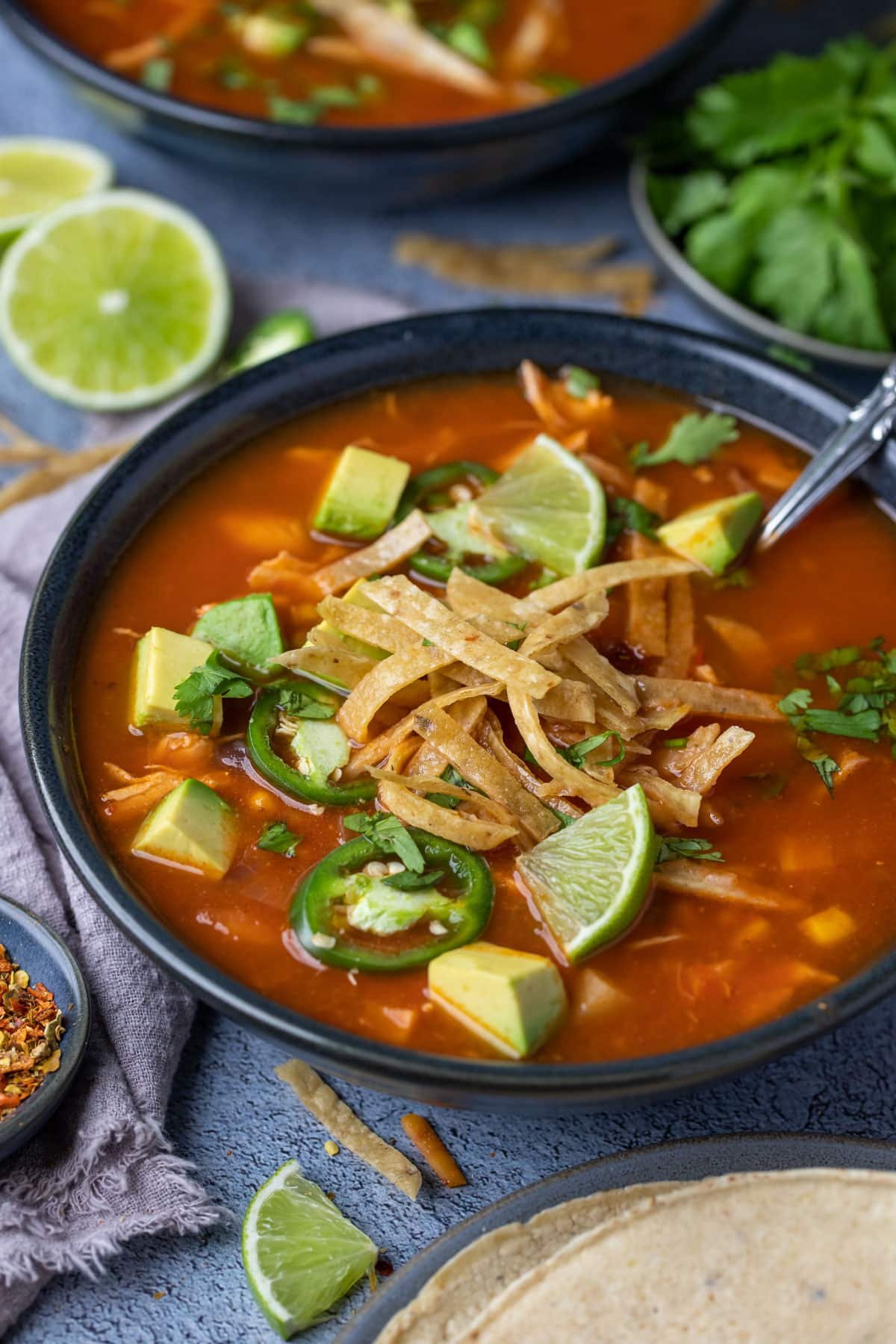 a bowl of soup topped with tortillas, avocado and slices of lime.