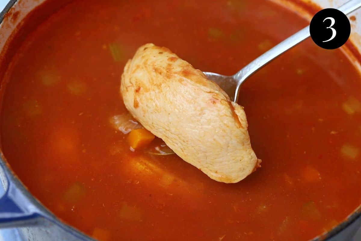 a piece of chicken being removed from a pot of soup.