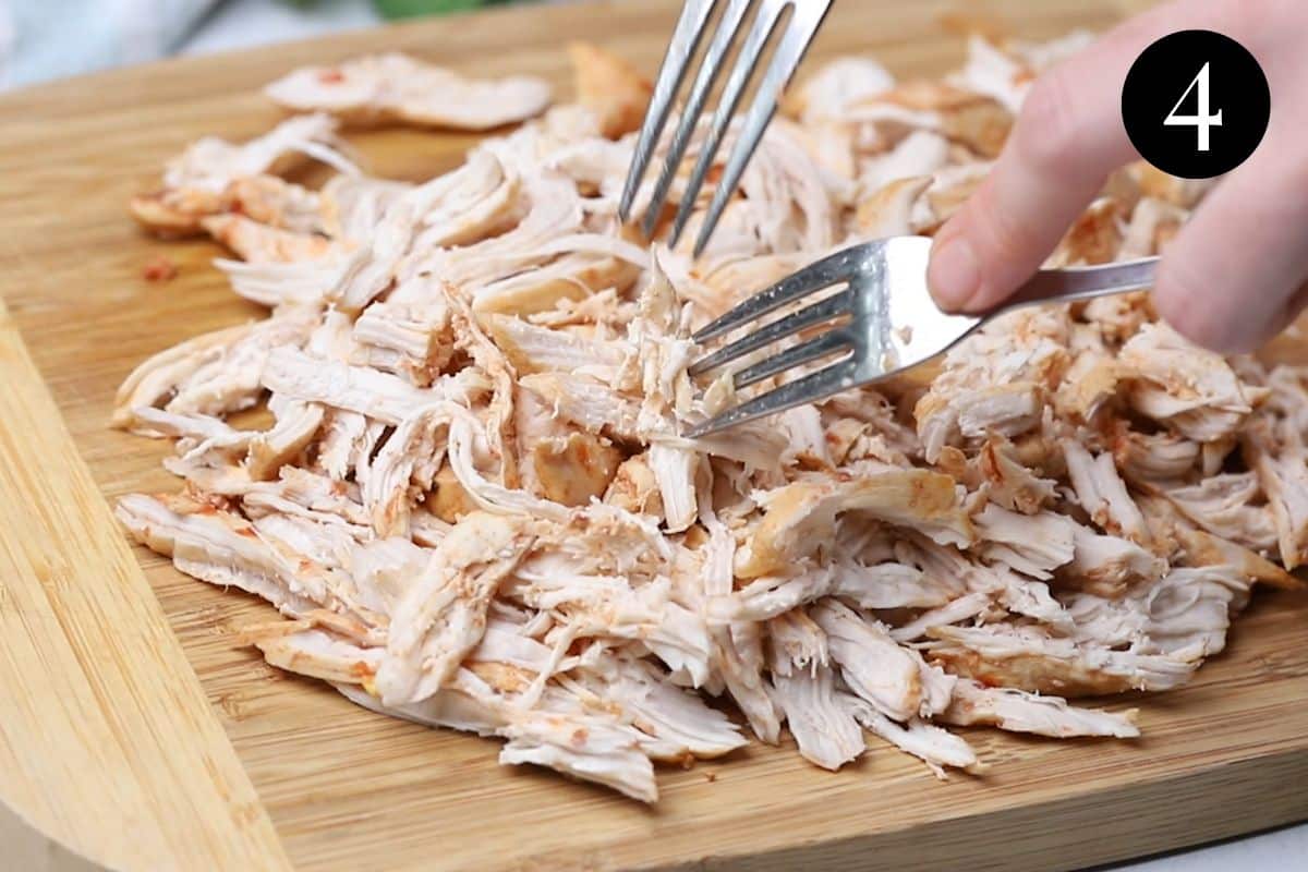 two forks shredded chicken on a board.