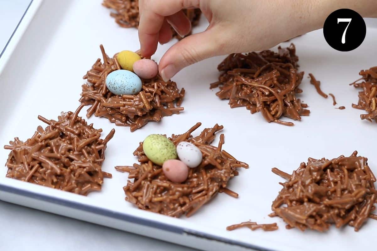 Easter eggs being added to the top of chocolate nests on a white tray.