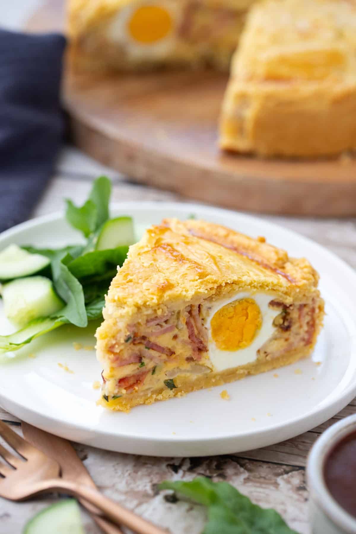 a slice of egg and bacon pie on a plate with salad.