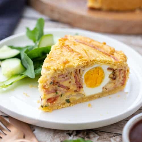 a slice of egg and bacon pie on a plate with salad.