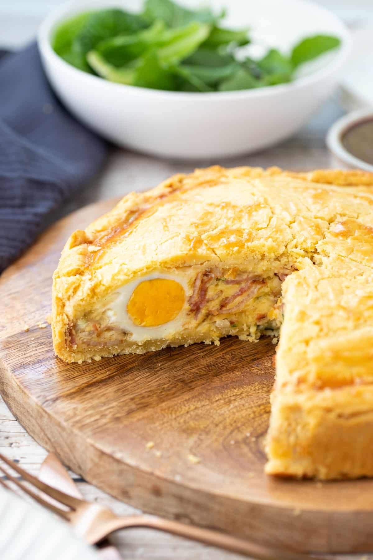 a pie on a wooden board on a table. The pie is sliced open, showing the filling.