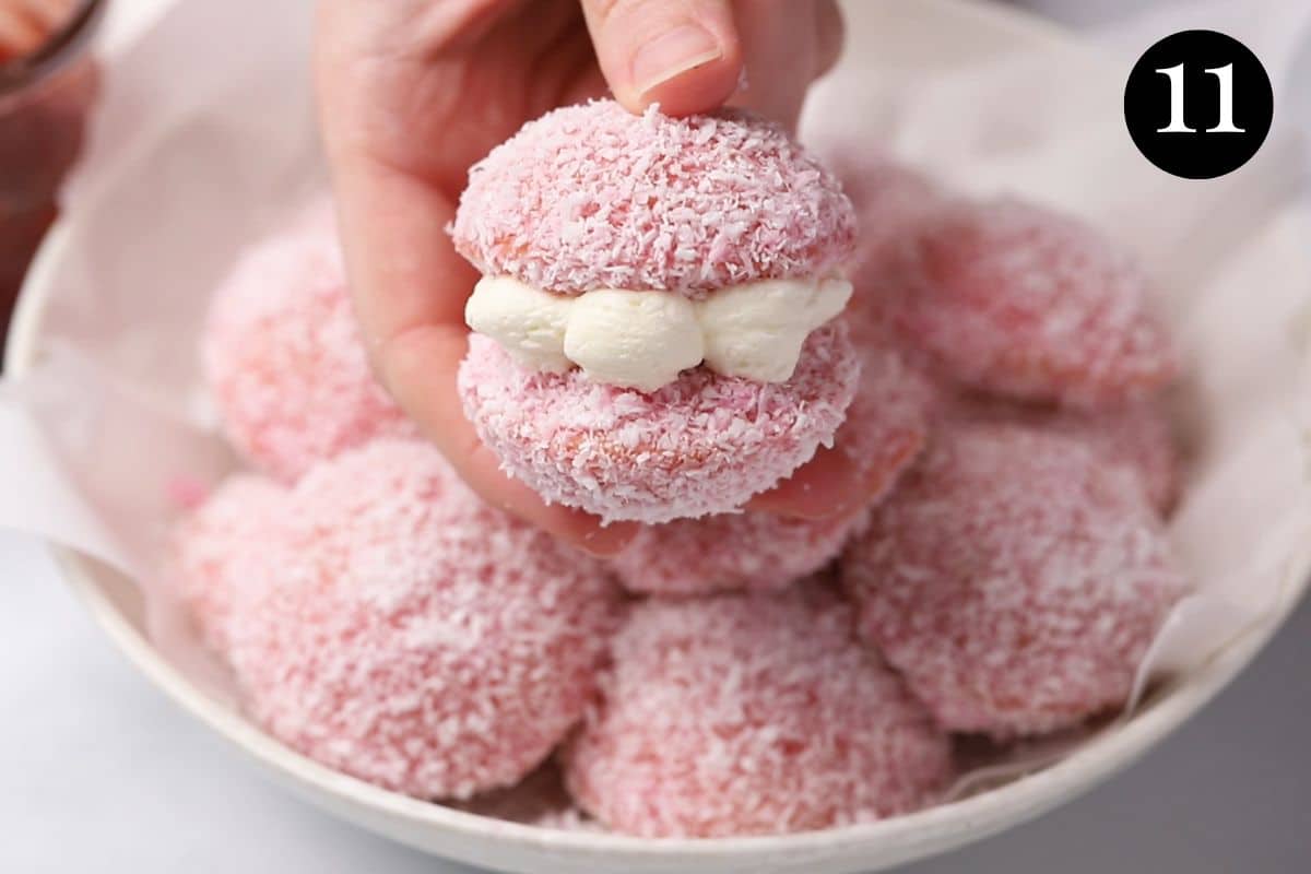 a hand holding a pink cake, filled with cream.