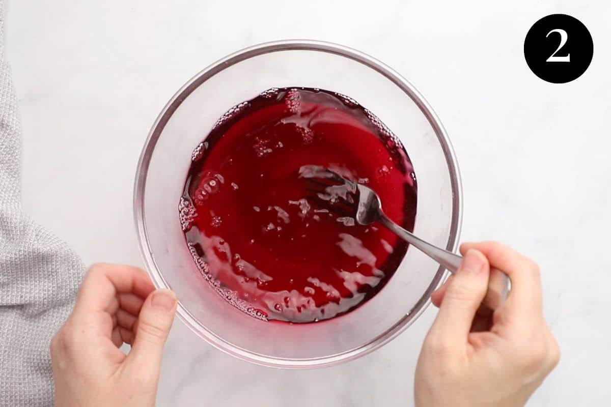 hands stirring pink jelly mixture in a bowl.