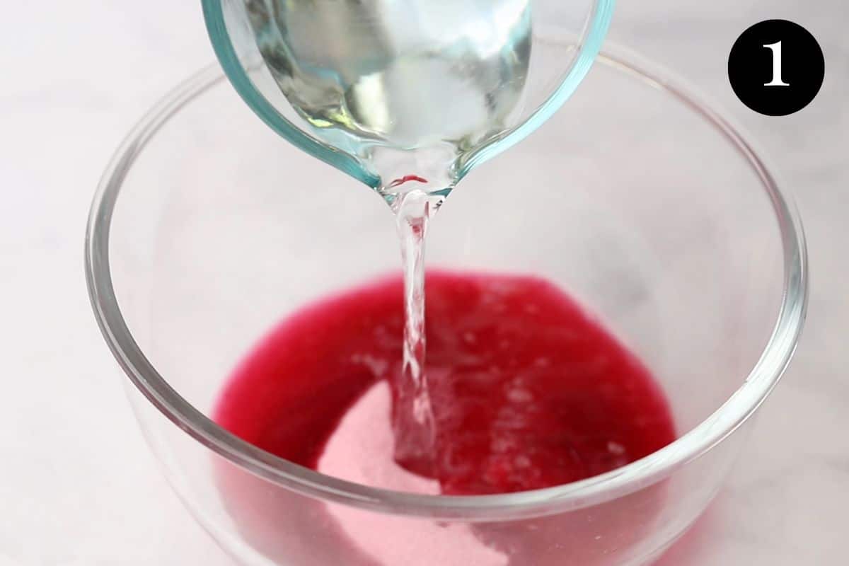 a jug of boiling water being poured over pink jelly crystals in a bowl.