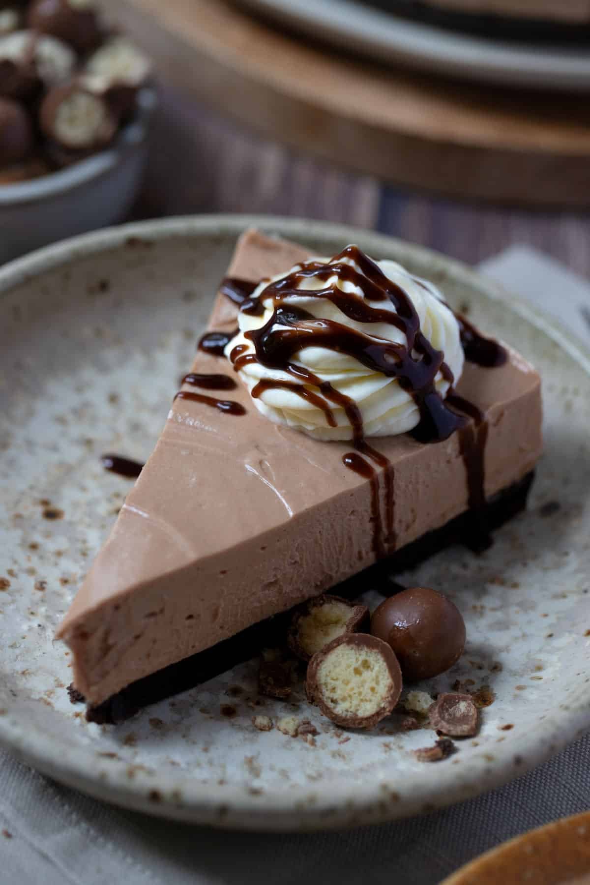 a slice of chocolate cheesecake on a plate with crushed chocolate and whipped cream.