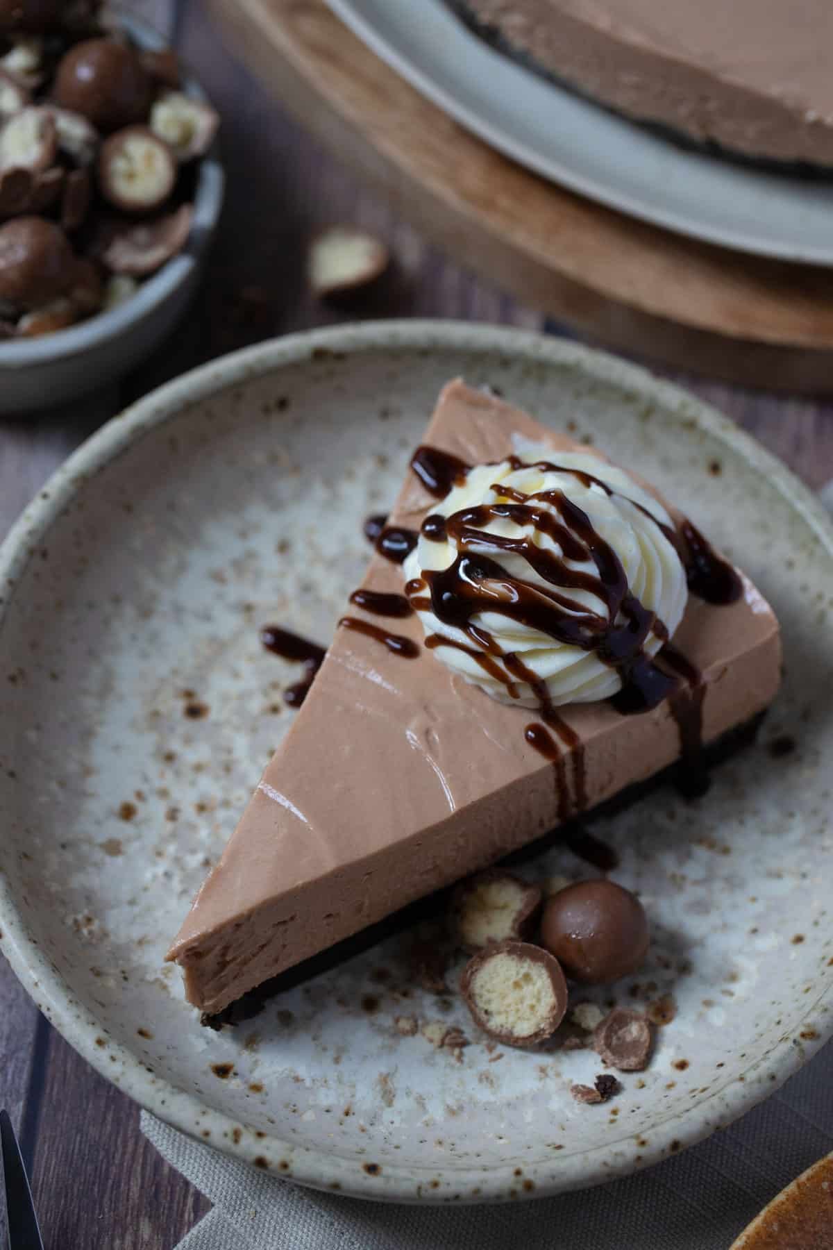 a slice of cheesecake on a plate topped with cream and chocolate.