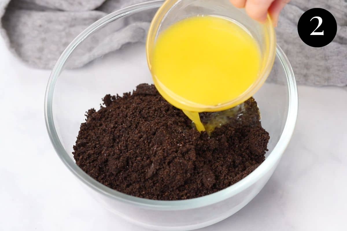 melted butter being poured over crushed biscuits in a bowl.