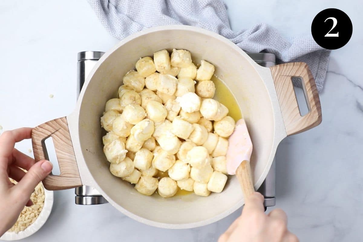 hands using a spatula to stir butter and marshmallow mixture in a pot.