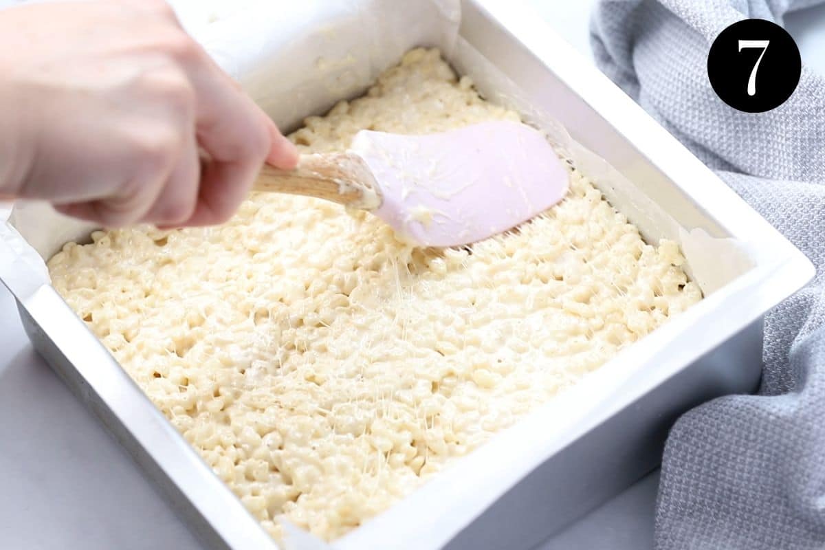 Rice Bubble slice mixture being pressed into a tin with a spatula.