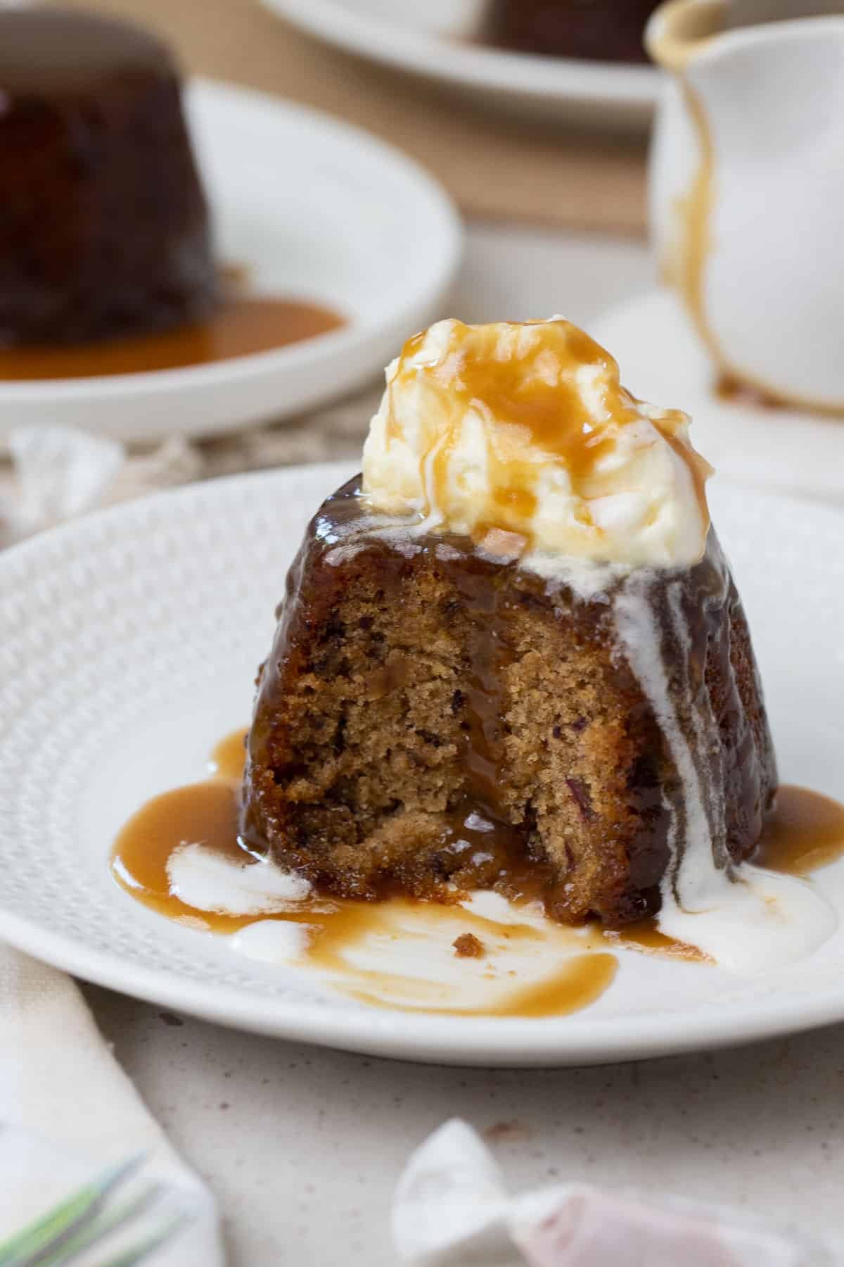 sticky date pudding on a plate topped with cream. The pudding is cut in half.