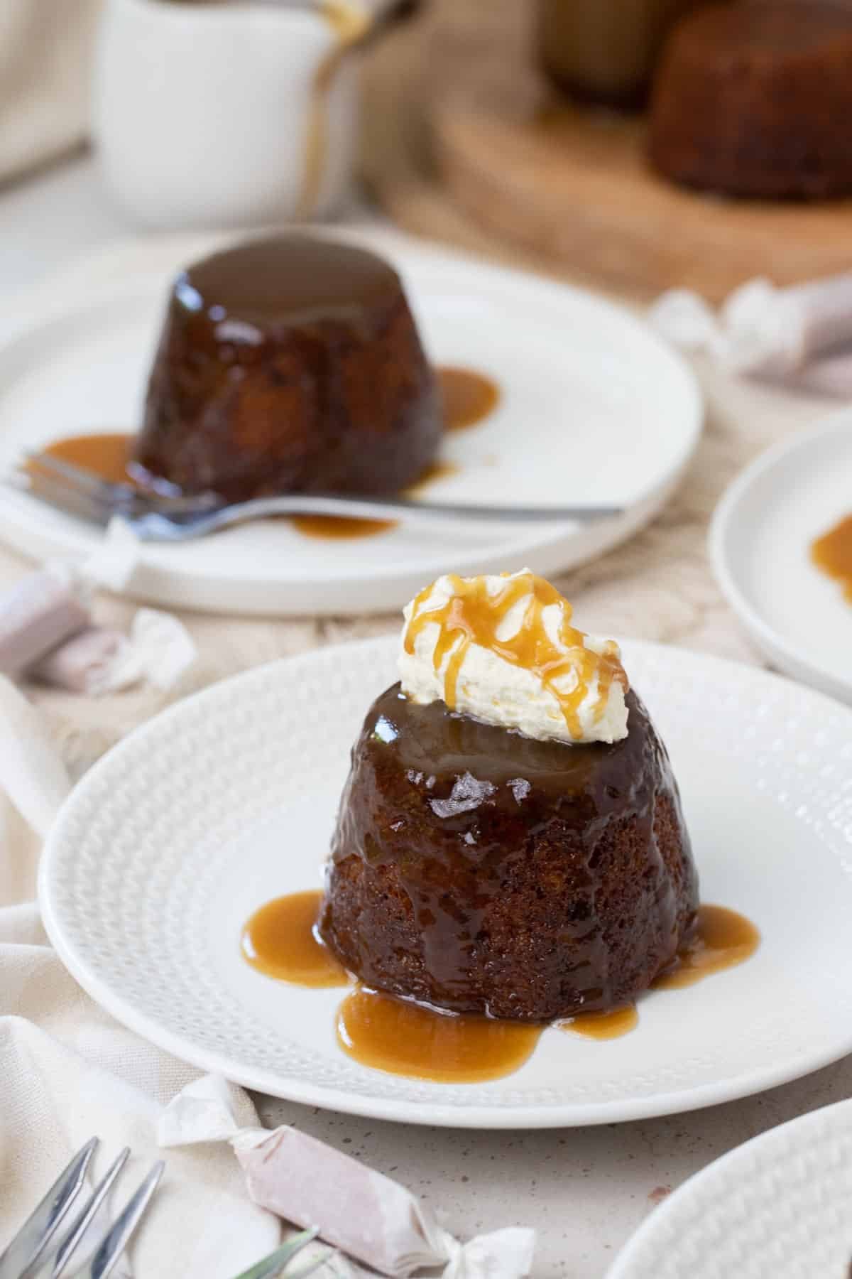 sticky date puddings on a plate topped with cream and caramel sauce.