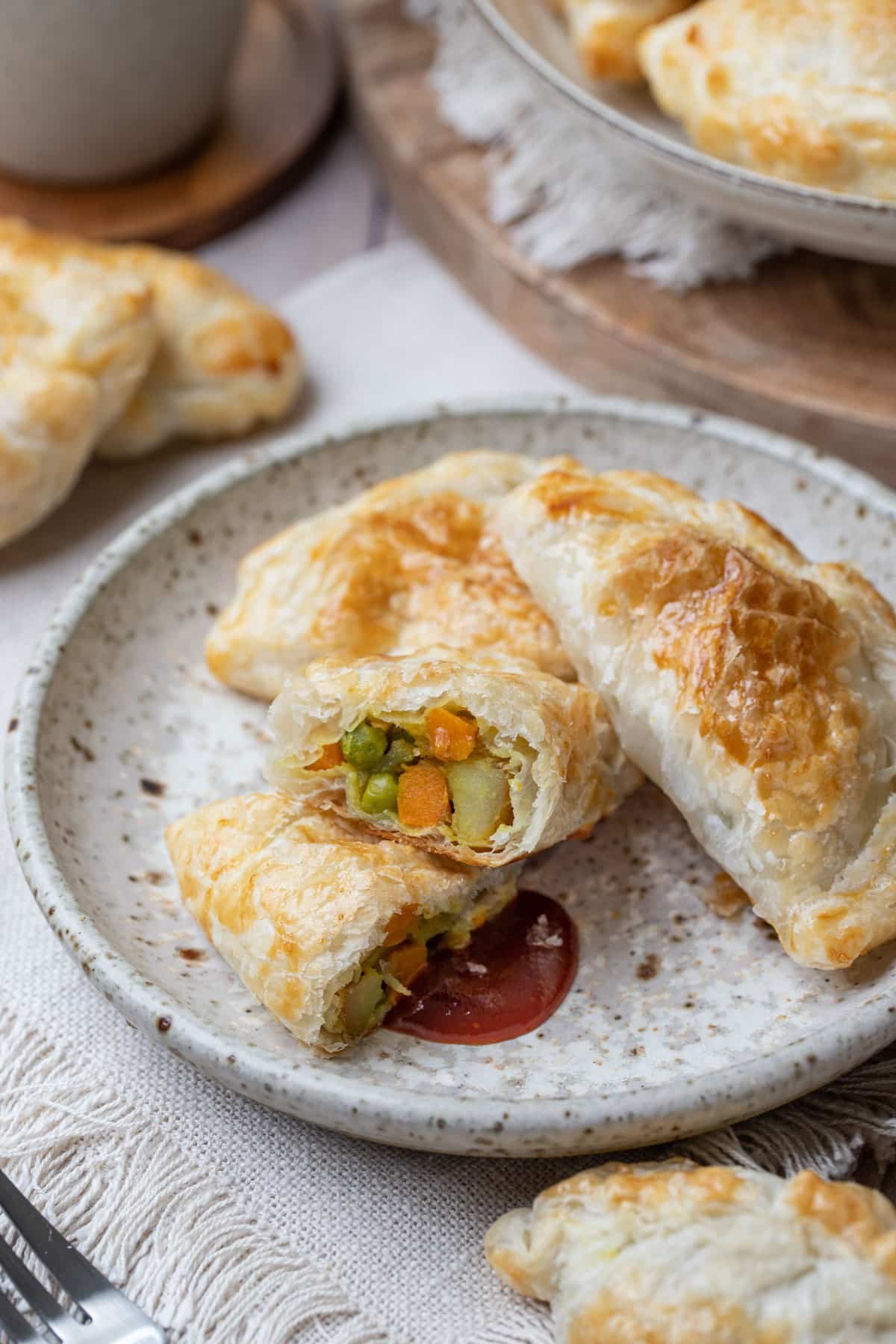 pasties on a plate, with tomato sauce. One is cut in half, showing the vegetable filling.