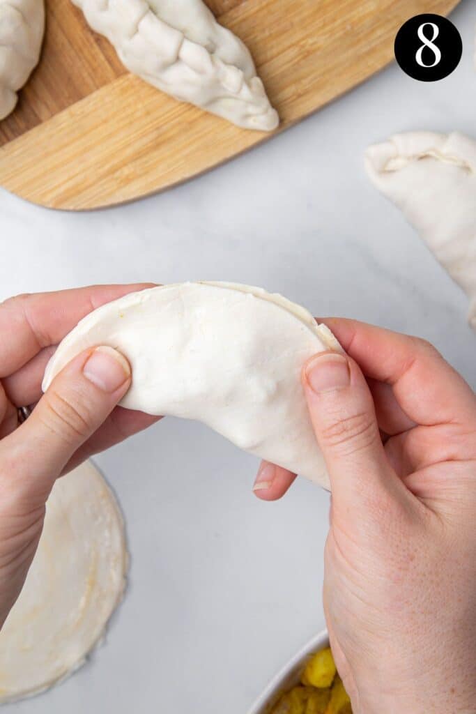 hands folding a filled pastry circle in half.