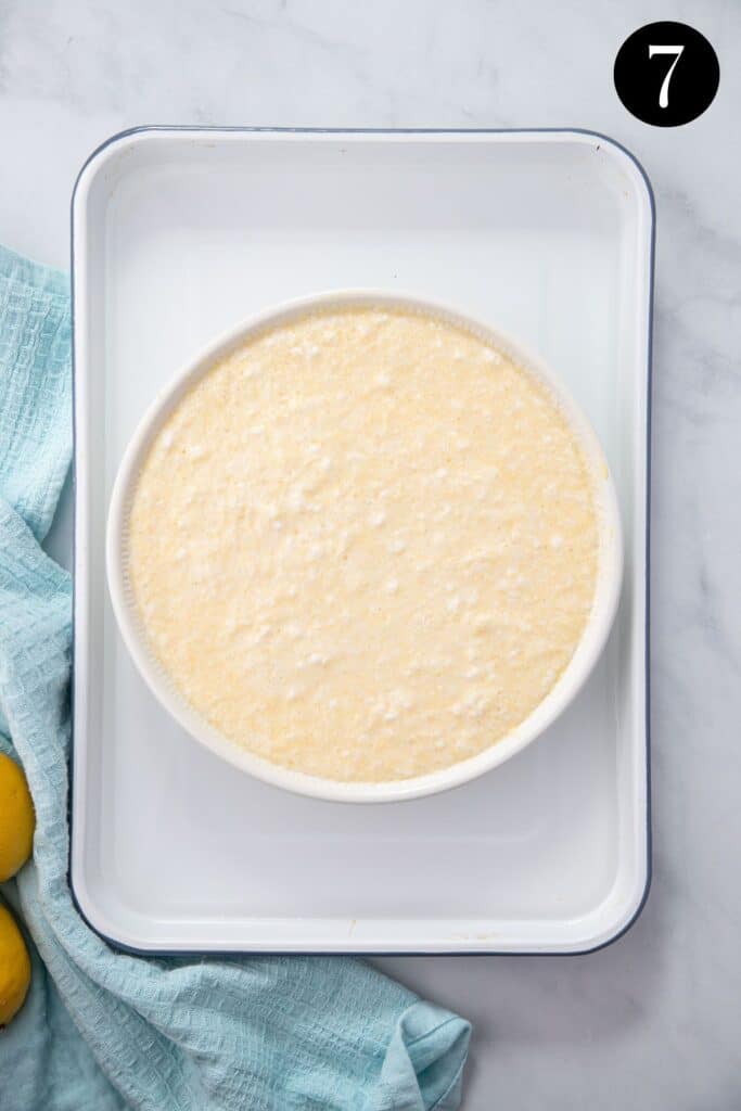 a baking dish filled with lemon pudding batter, sitting in a white baking tray.