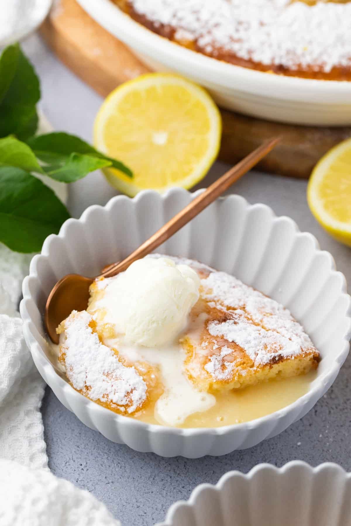 a bowl of lemon delicious pudding and a spoon, topped with a scoop of ice cream