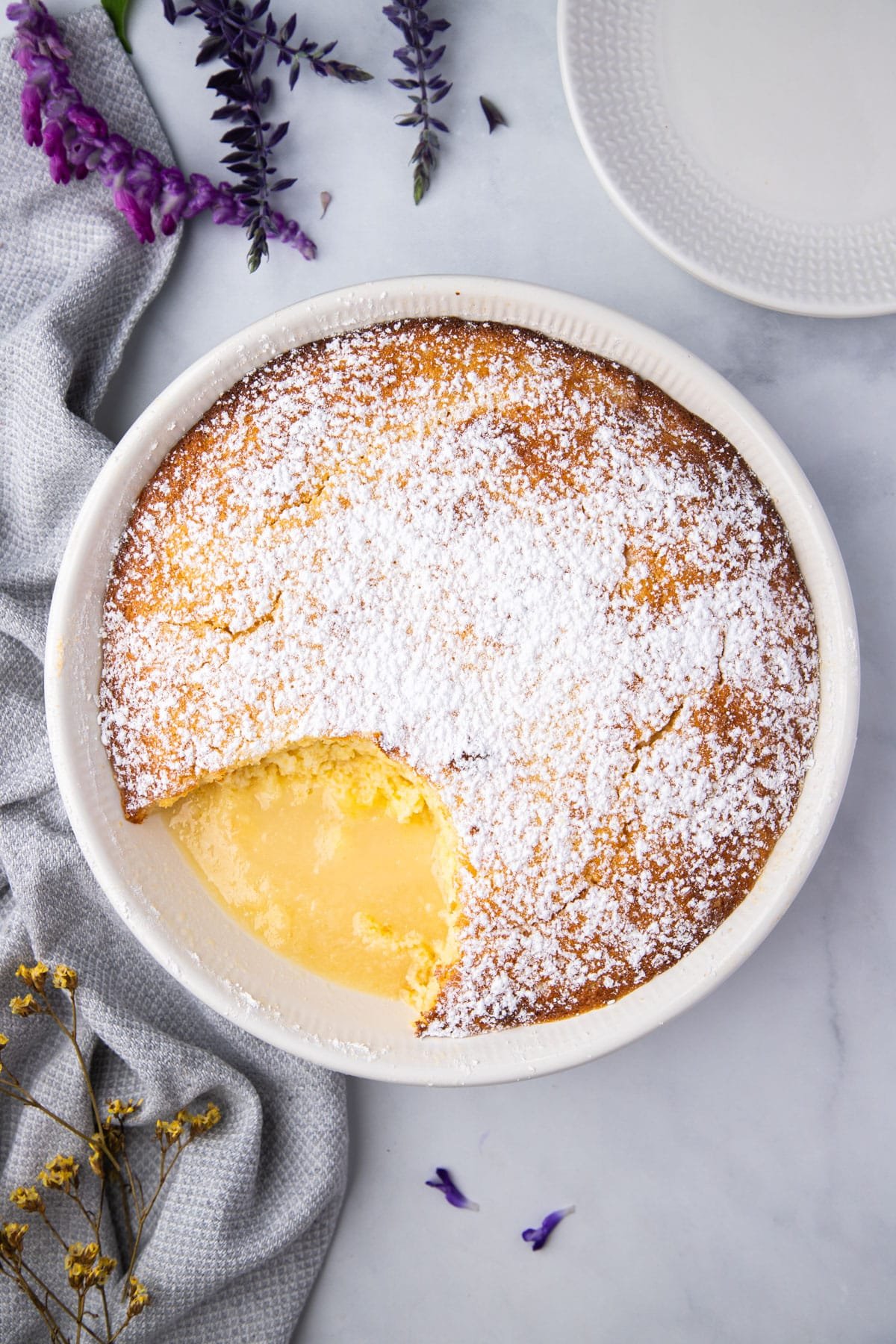 lemon sponge pudding in a large white dish, surrounded by flowers.