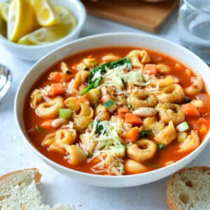 a bowl of tortellini soup topped with cheese and herbs.