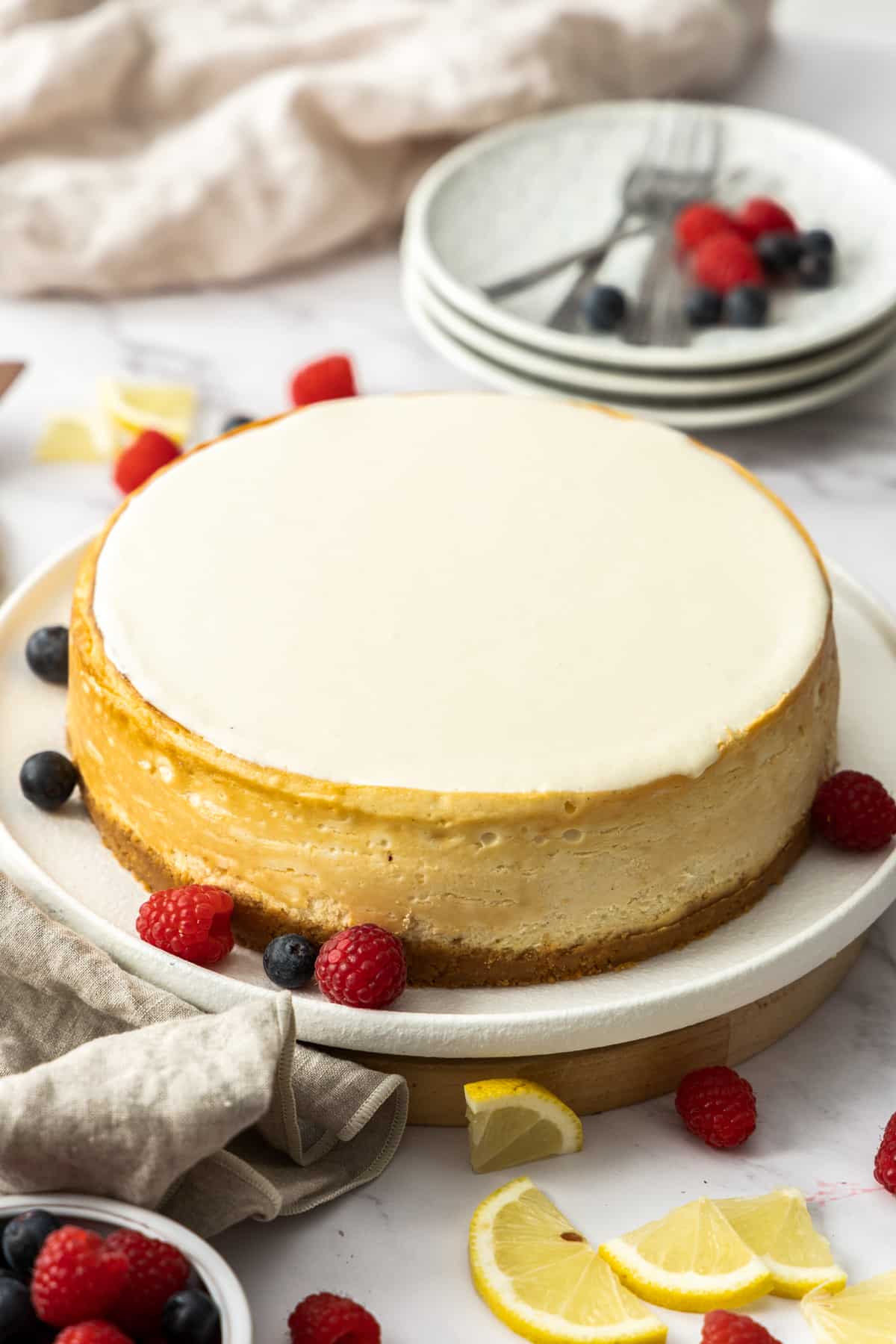 cheesecake with a sour cream topping layer, on a plate with fresh berries.