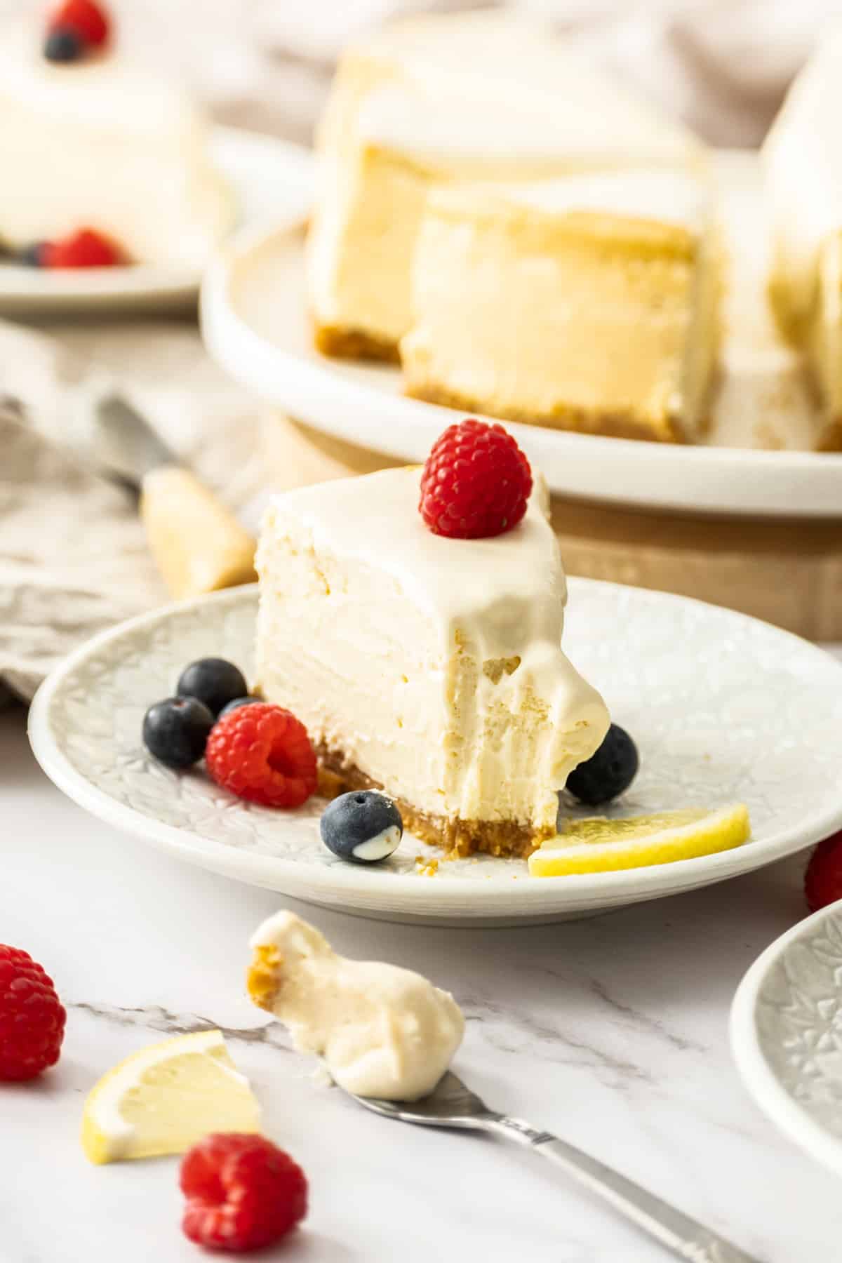 a slice of cheesecake on a plate with a bite missing. It's surrounded by fresh berries.