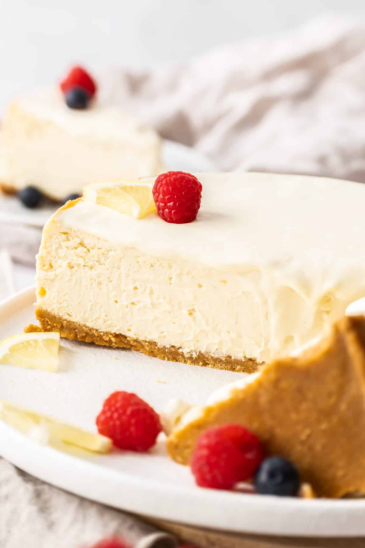 a sliced New York cheesecake on a white plate, topped with fresh berries.