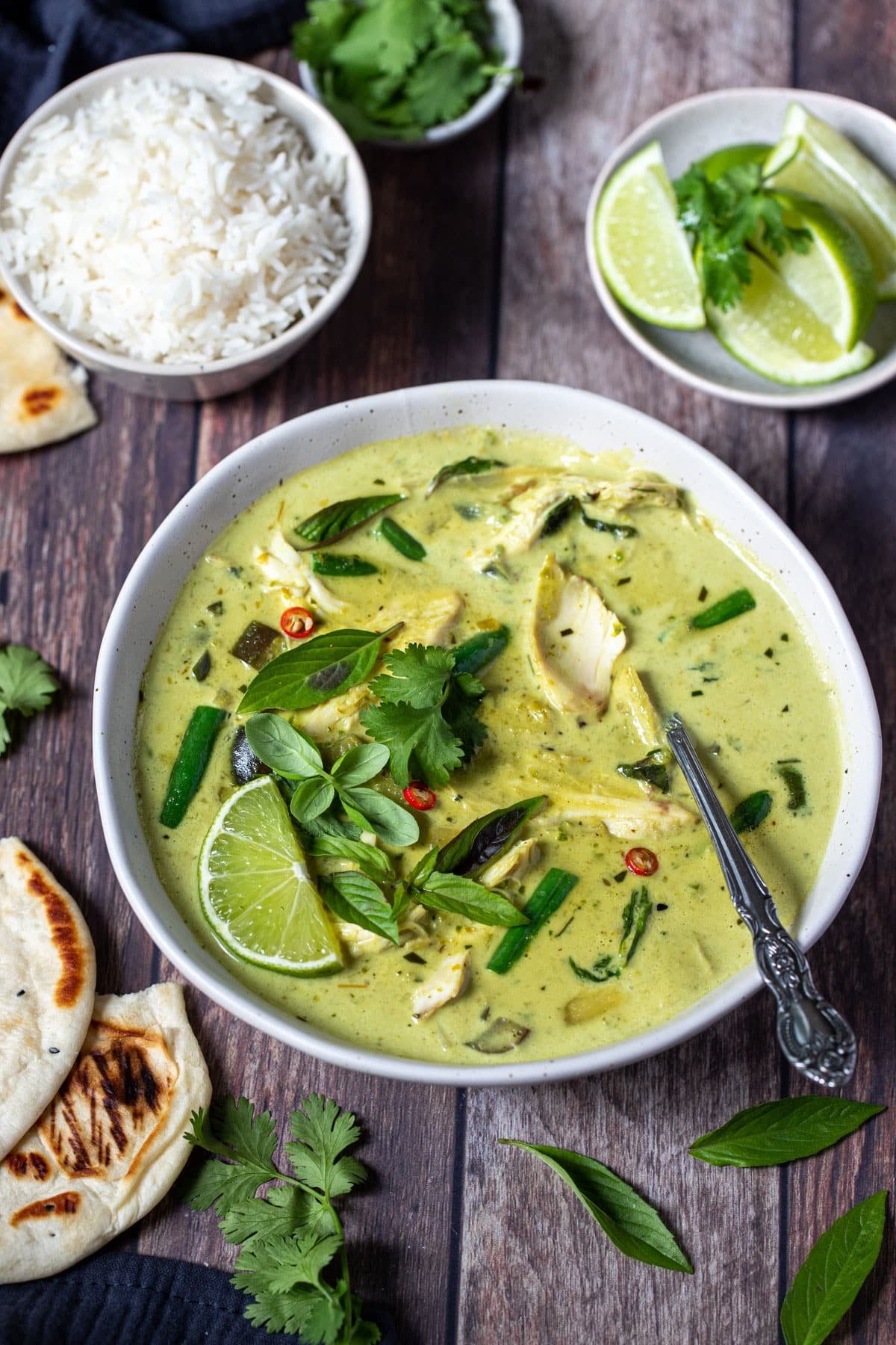 a bowl of green curry on a table with chicken and vegetables.