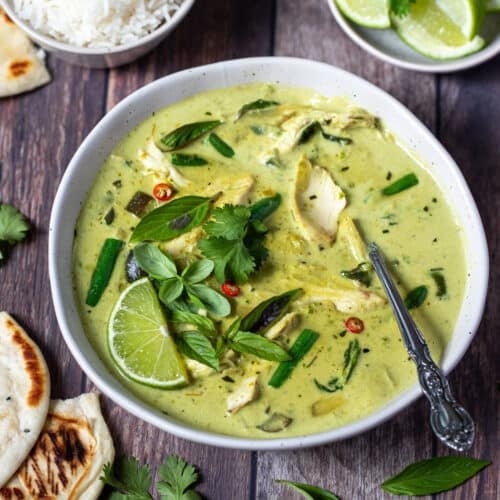 a bowl of green chicken curry, topped with lime and herbs.
