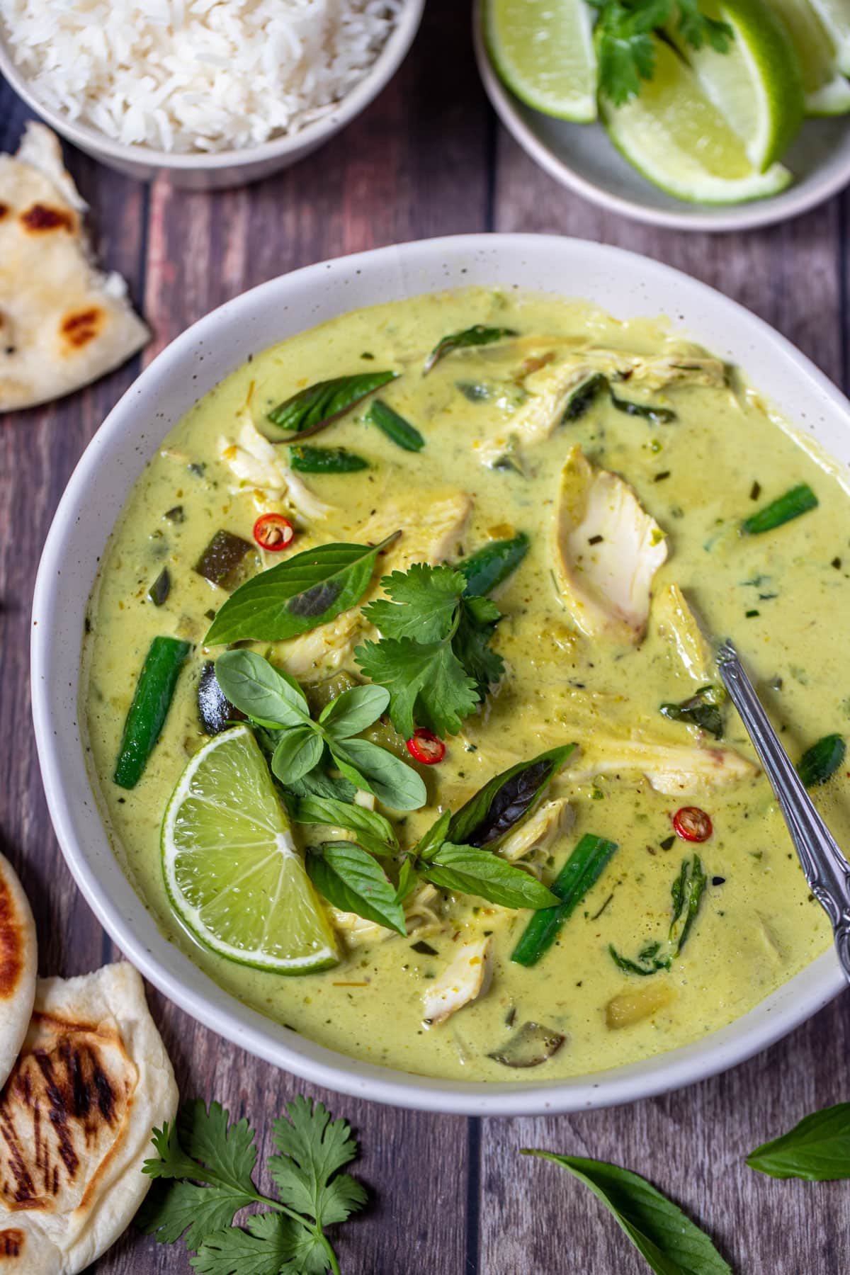 a bowl of green curry topped with lime and Thai basil.