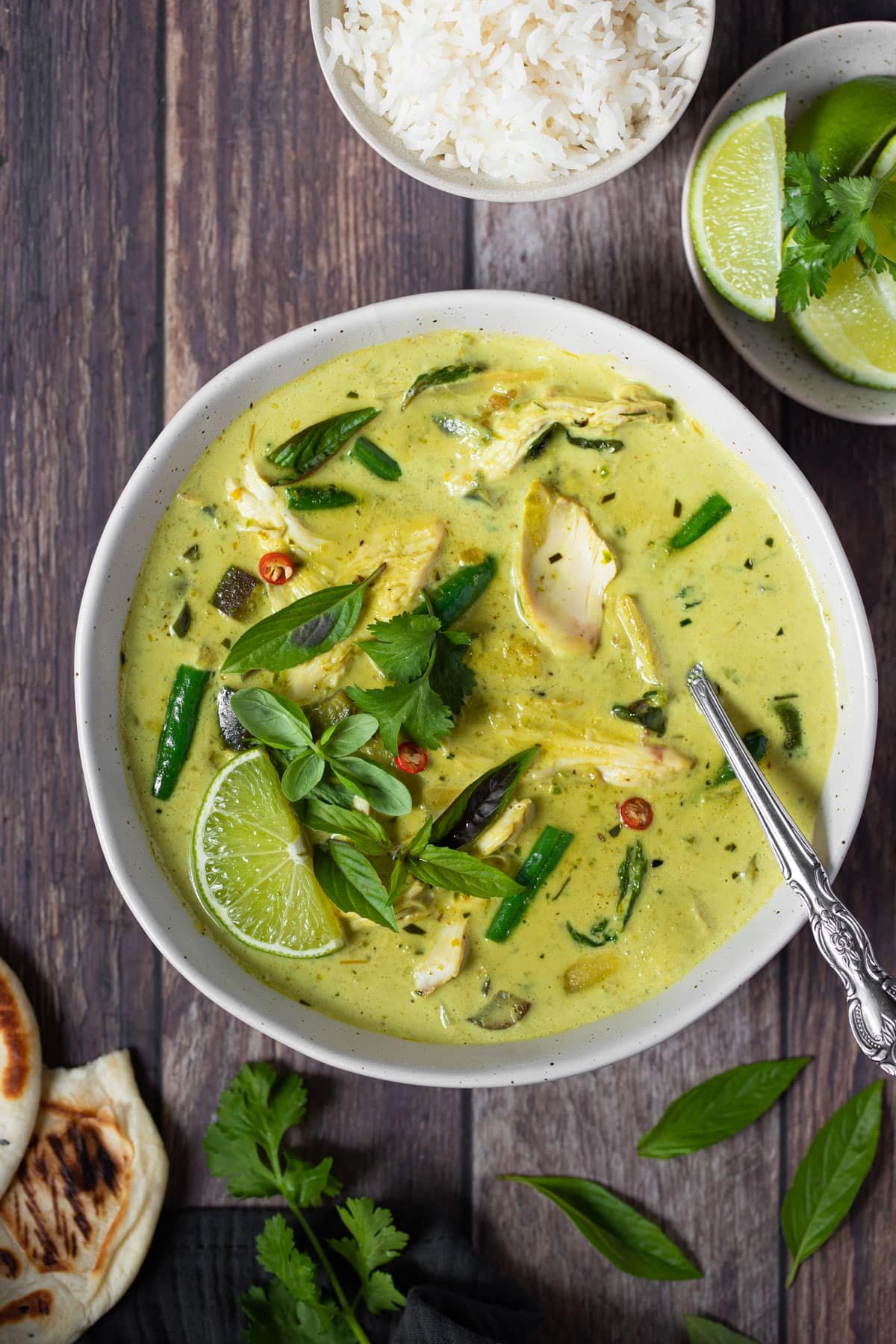 a bowl of curry topped with lime and fresh herbs on a table.