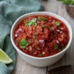 a bowl of salsa on a table with corn chips and lime wedges.