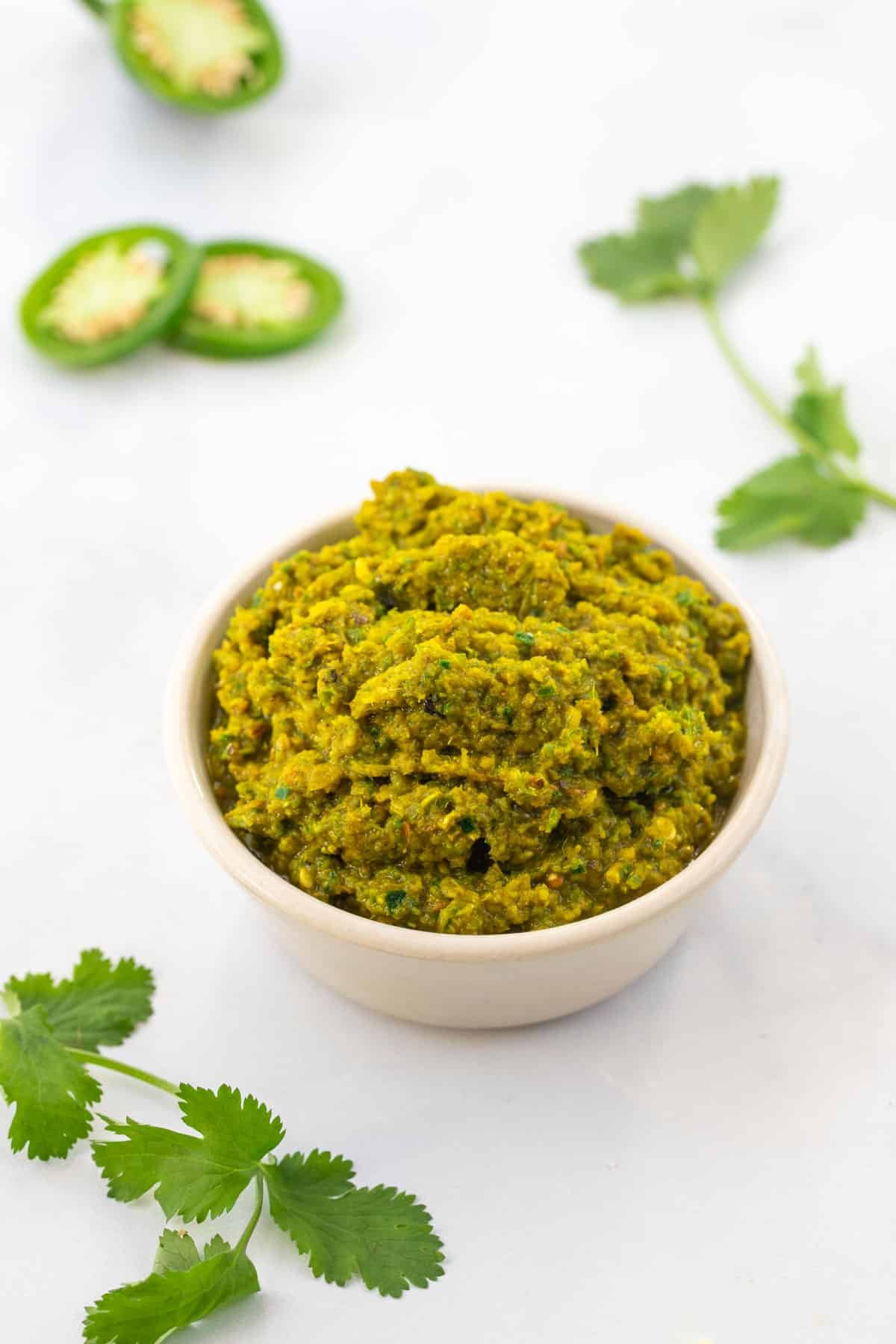 a bowl of green curry paste on a table with coriander and sliced chillies.